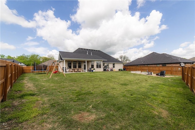 back of house with a lawn, a trampoline, a fenced backyard, and a patio area