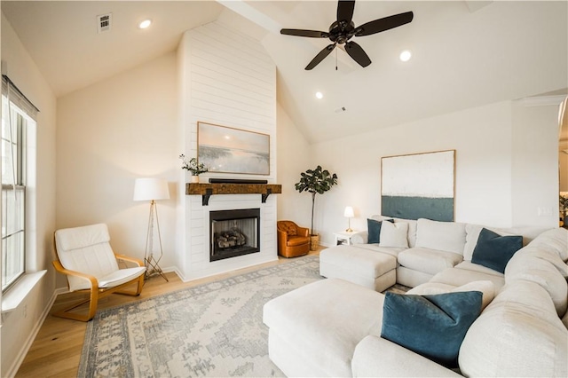 living area with a large fireplace, lofted ceiling, a ceiling fan, baseboards, and wood finished floors