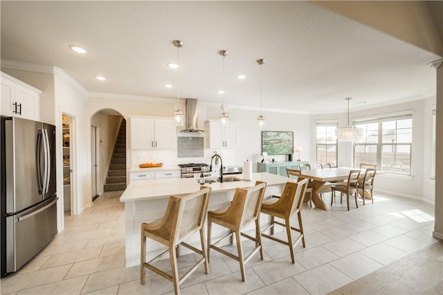 kitchen featuring appliances with stainless steel finishes, wall chimney range hood, and ornamental molding