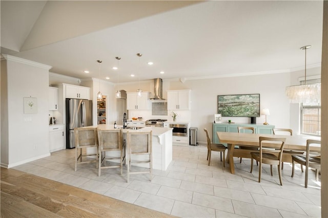 kitchen featuring a kitchen island with sink, stainless steel appliances, light countertops, wall chimney exhaust hood, and crown molding