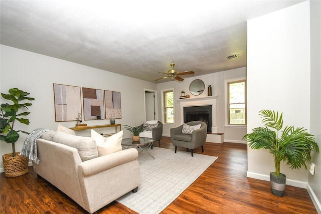 living room with ceiling fan, a fireplace with raised hearth, visible vents, dark wood-style floors, and baseboards