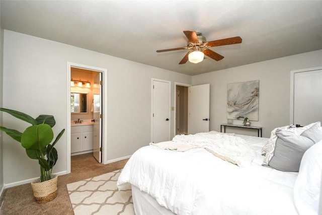 bedroom with a sink, light colored carpet, baseboards, a ceiling fan, and ensuite bath
