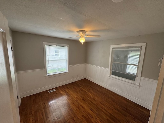 spare room with a healthy amount of sunlight, a wainscoted wall, and dark wood finished floors