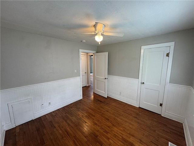 unfurnished bedroom with hardwood / wood-style floors, wainscoting, and a ceiling fan