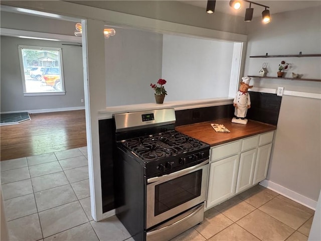 kitchen featuring baseboards, butcher block counters, light tile patterned floors, white cabinetry, and stainless steel range with gas cooktop