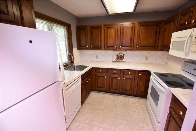 kitchen with tile counters, white appliances, decorative backsplash, and a sink
