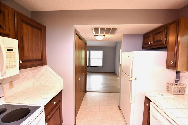 kitchen featuring visible vents, backsplash, tile countertops, and white microwave