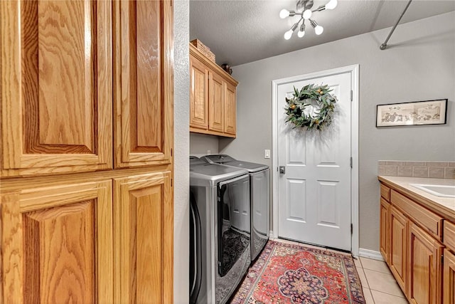 washroom with separate washer and dryer, cabinet space, a sink, a textured ceiling, and light tile patterned flooring