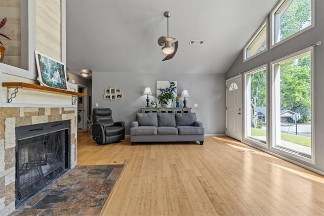 living room with a fireplace, high vaulted ceiling, a ceiling fan, visible vents, and hardwood / wood-style flooring