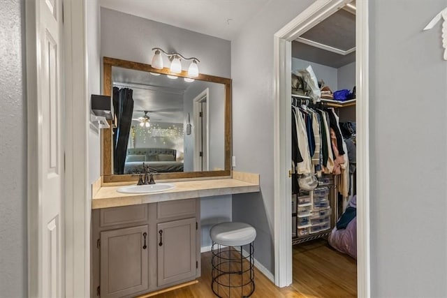 bathroom with wood finished floors, ensuite bath, ceiling fan, vanity, and a walk in closet