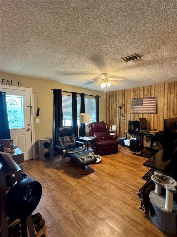 living room with a textured ceiling, visible vents, a ceiling fan, and light wood-type flooring