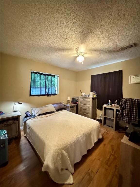 bedroom with visible vents, ceiling fan, a textured ceiling, and dark wood-type flooring
