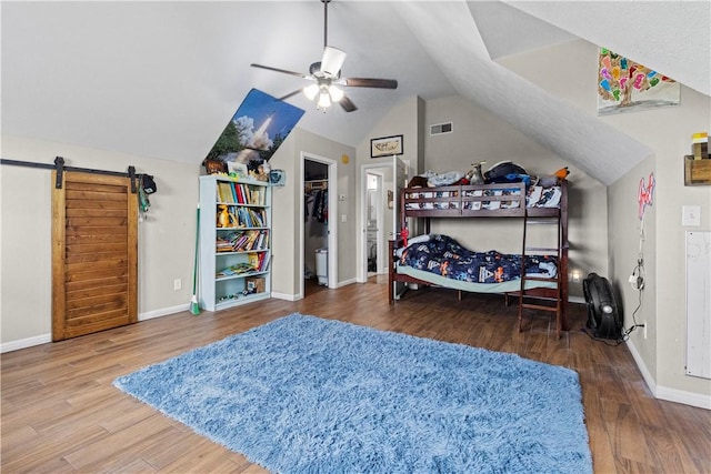 bedroom featuring visible vents, a barn door, baseboards, vaulted ceiling, and wood finished floors