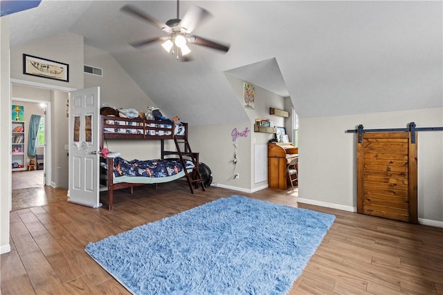 bedroom with wood finished floors, a barn door, vaulted ceiling, and baseboards