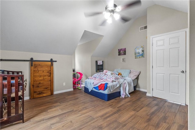 bedroom featuring lofted ceiling, visible vents, a barn door, baseboards, and wood finished floors