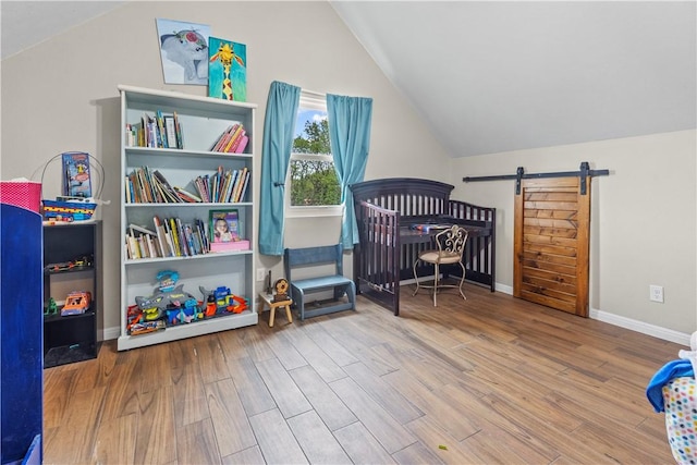 bedroom with lofted ceiling, wood finished floors, baseboards, and a barn door