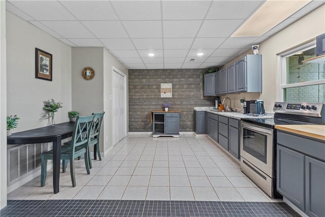 kitchen with light tile patterned floors, stainless steel electric range oven, gray cabinetry, and a drop ceiling
