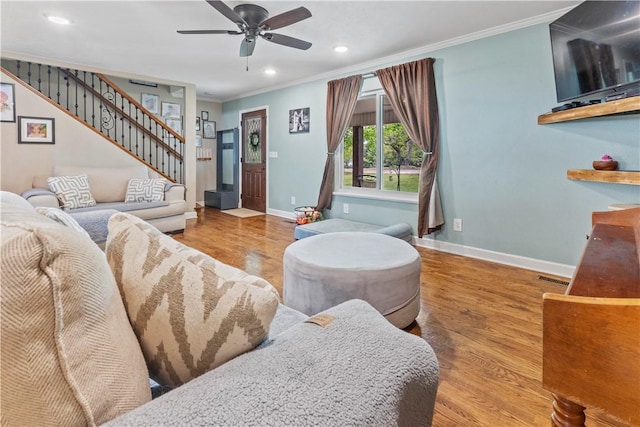 living room featuring crown molding, ceiling fan, baseboards, wood finished floors, and stairs