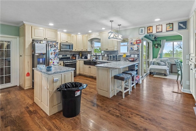 kitchen featuring tasteful backsplash, appliances with stainless steel finishes, ornamental molding, cream cabinets, and a peninsula