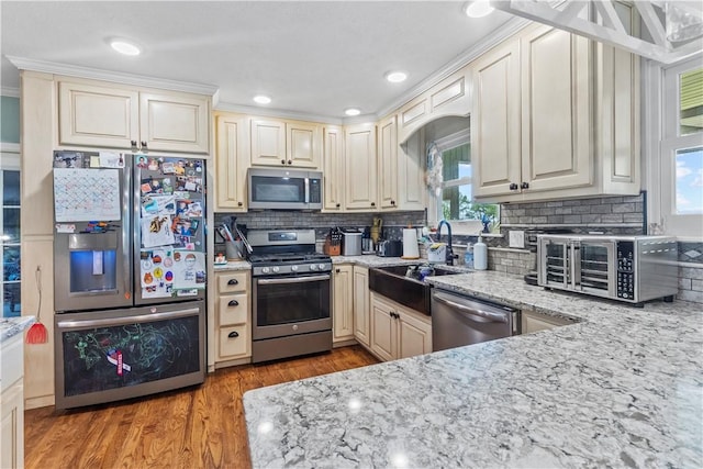 kitchen featuring light stone countertops, a sink, decorative backsplash, light wood-style flooring, and appliances with stainless steel finishes