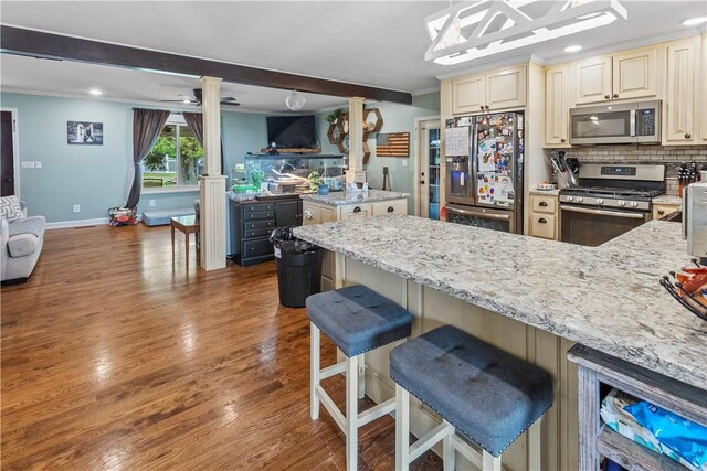 kitchen featuring stainless steel appliances, cream cabinets, light stone counters, a peninsula, and wood finished floors