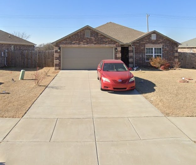 ranch-style house featuring brick siding, fence, driveway, and an attached garage