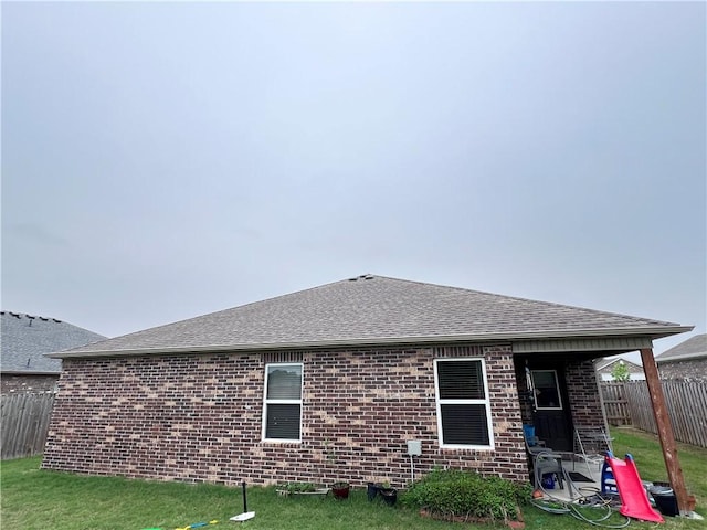 back of house with brick siding, fence, a shingled roof, and a yard