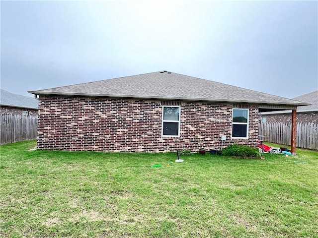 back of house with a lawn, roof with shingles, brick siding, and fence private yard