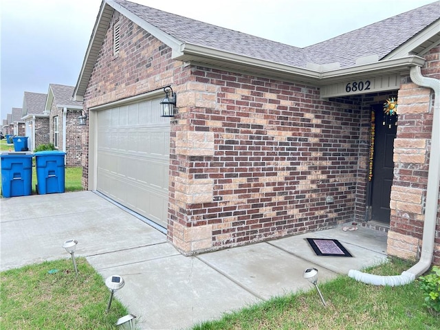 view of property exterior with driveway, a shingled roof, brick siding, and a garage
