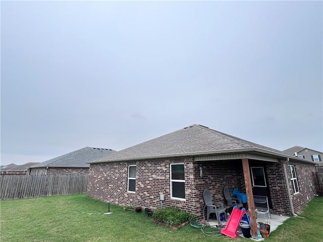 rear view of house featuring a lawn, a patio area, brick siding, and a fenced backyard