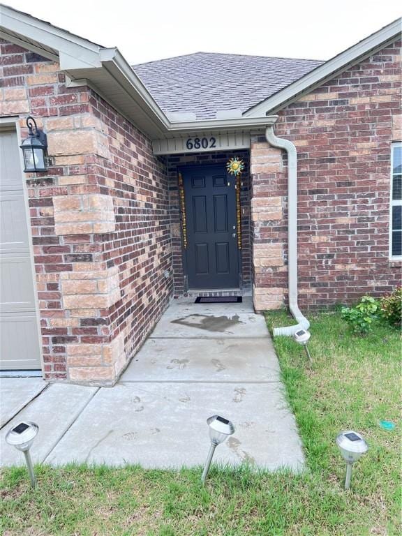 doorway to property featuring brick siding and roof with shingles