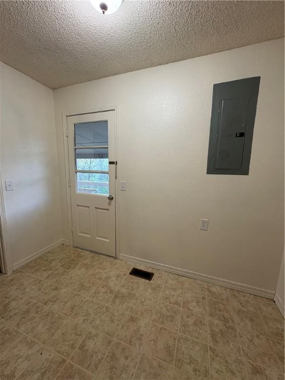 doorway with baseboards, visible vents, a textured ceiling, and electric panel