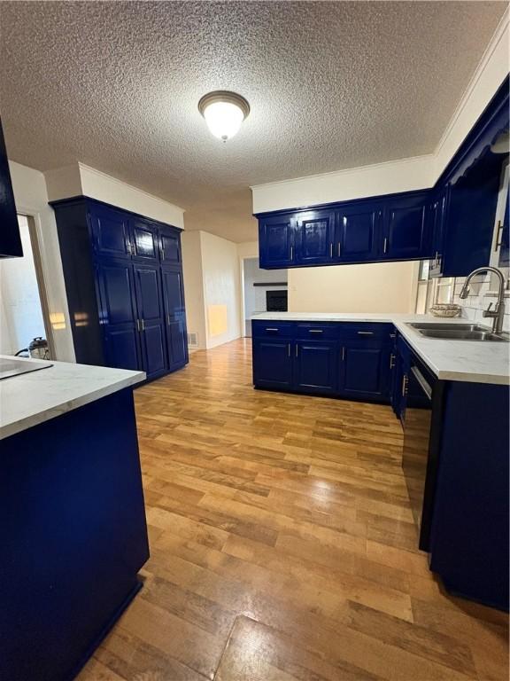 kitchen featuring a textured ceiling, light wood-style flooring, a sink, blue cabinetry, and dishwasher