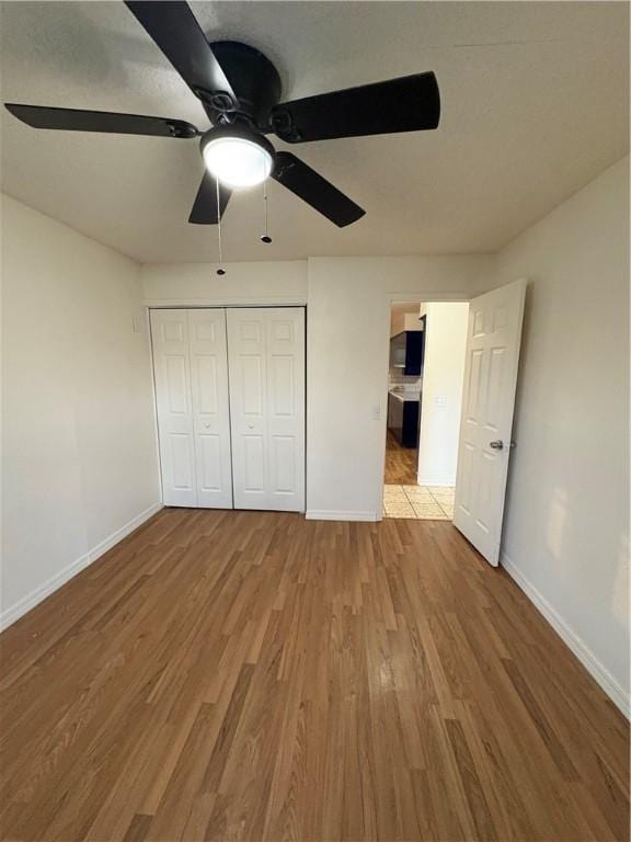 unfurnished bedroom with wood finished floors, ceiling fan, a closet, and baseboards