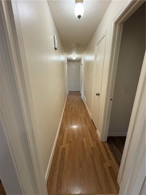 hall with a textured ceiling, wood finished floors, and baseboards