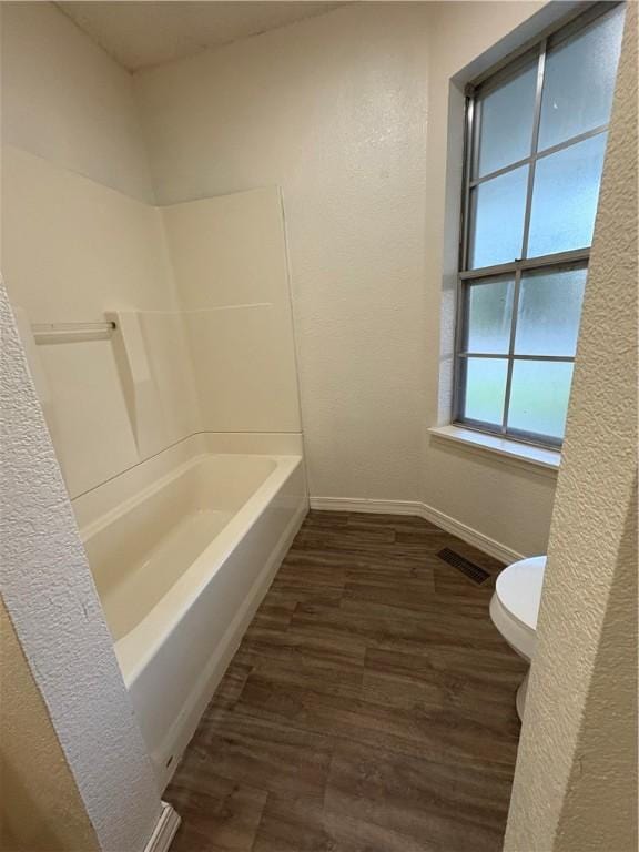 bathroom featuring toilet, visible vents, a textured wall, baseboards, and wood finished floors