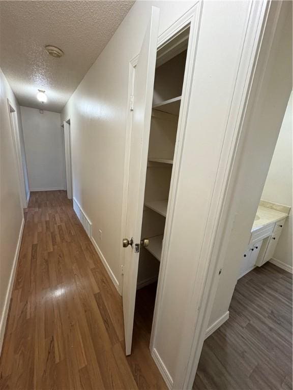 hallway featuring a textured ceiling, visible vents, wood finished floors, and baseboards