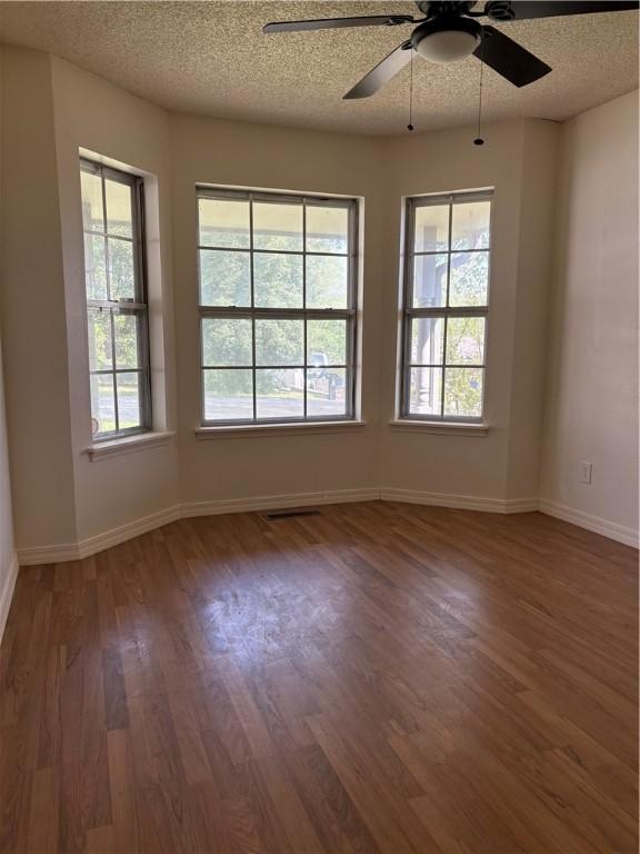 unfurnished room with a ceiling fan, visible vents, baseboards, a textured ceiling, and wood finished floors