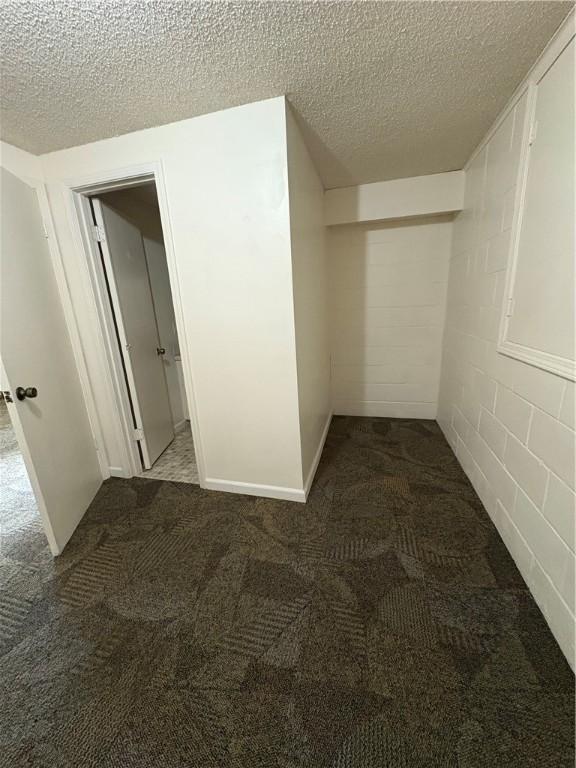 interior space with concrete block wall, a textured ceiling, and dark carpet