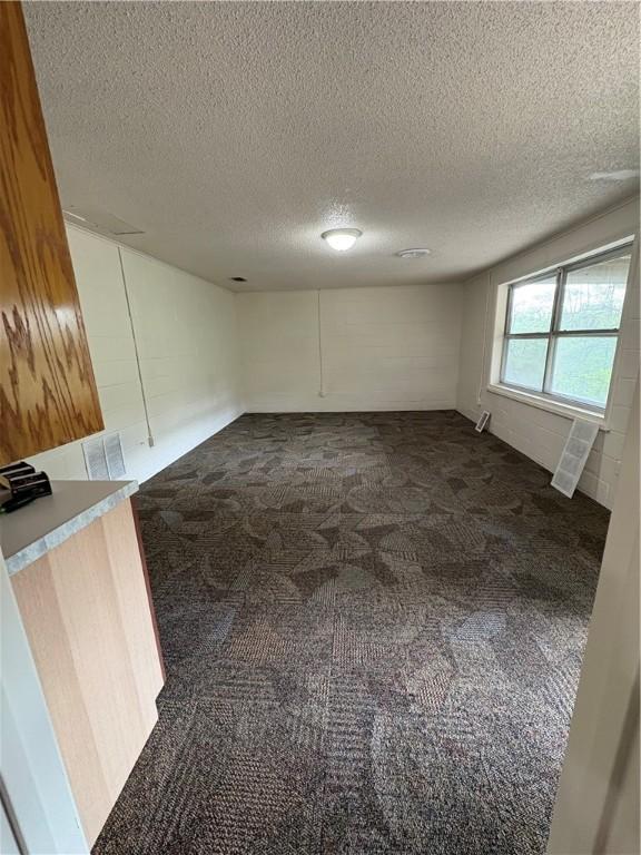 spare room featuring visible vents, dark colored carpet, and a textured ceiling