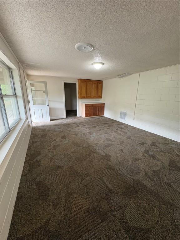 unfurnished living room with a textured ceiling, visible vents, concrete block wall, and carpet floors