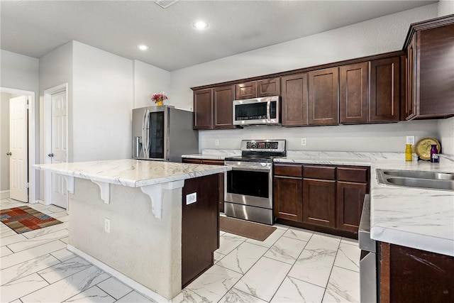 kitchen featuring recessed lighting, a sink, stainless steel appliances, marble finish floor, and a kitchen island