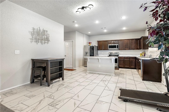 kitchen with appliances with stainless steel finishes, light countertops, a center island, baseboards, and marble finish floor