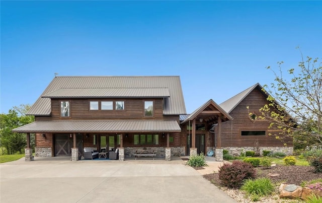 log cabin with covered porch, concrete driveway, metal roof, and stone siding
