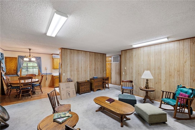 living area with a textured ceiling, wood walls, visible vents, a chandelier, and wood finished floors