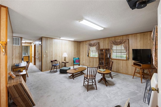 sitting room featuring wooden walls, a textured ceiling, visible vents, and carpet