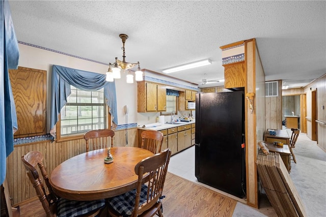 dining space with wood walls, a textured ceiling, a wainscoted wall, and light wood finished floors