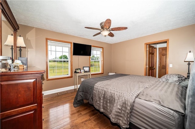 bedroom with ceiling fan, wood-type flooring, baseboards, visible vents, and a textured ceiling