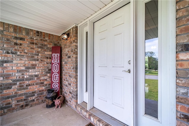 doorway to property with a porch and brick siding