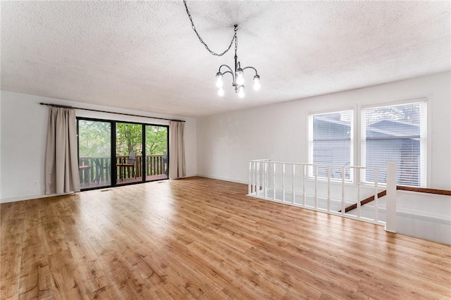unfurnished living room with a textured ceiling, a notable chandelier, baseboards, and light wood-style floors
